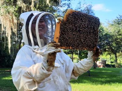 student with protective gear holding bea hive